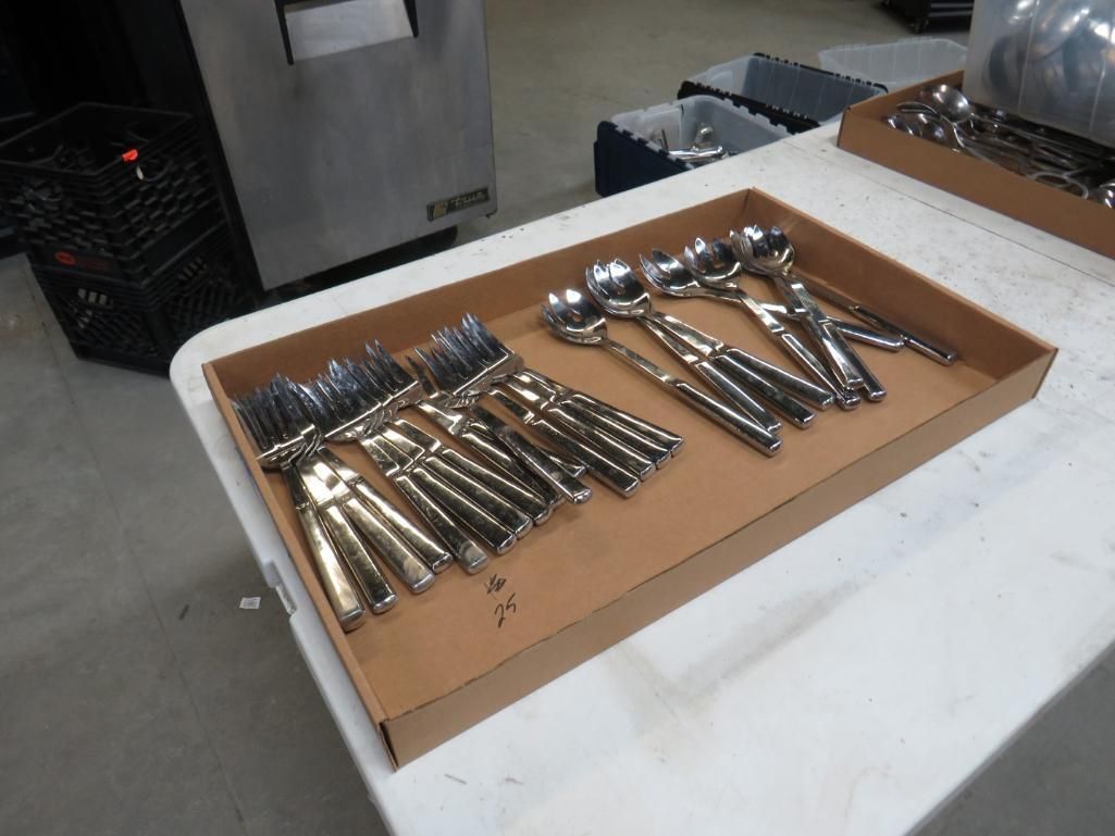 Utensils in cardboard trays on a white table. Forks and spoons are visible.