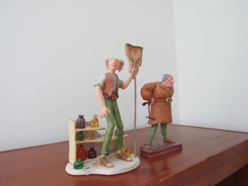 Figurines of two cartoon characters on a wooden surface. One holds a net, other stands with a staff.