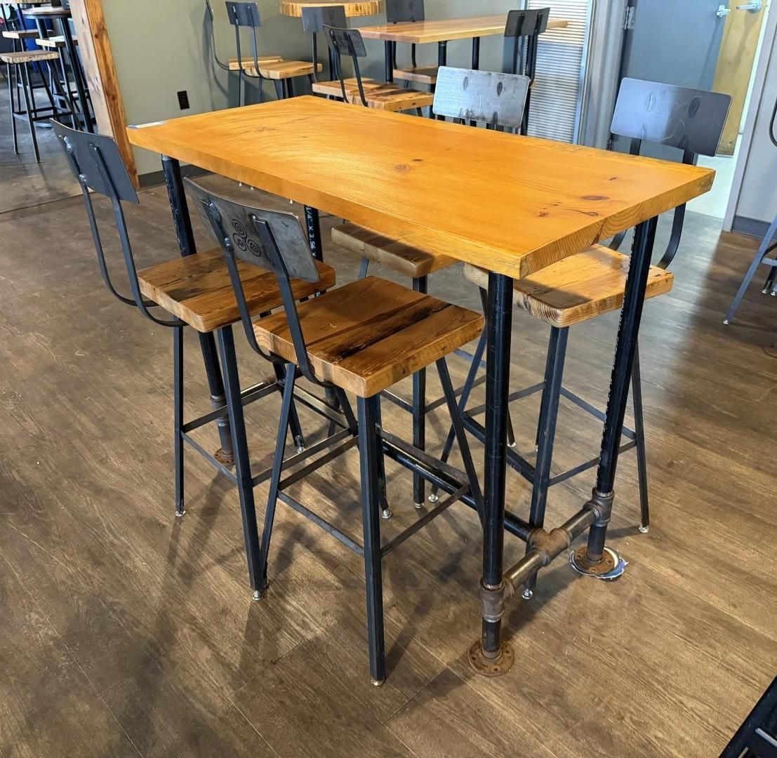 Bar-height table with four stools, all made of wood and black metal, set on a wood floor.