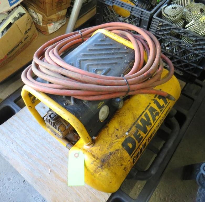 Yellow DeWalt air compressor with a coiled red hose on a wooden surface.