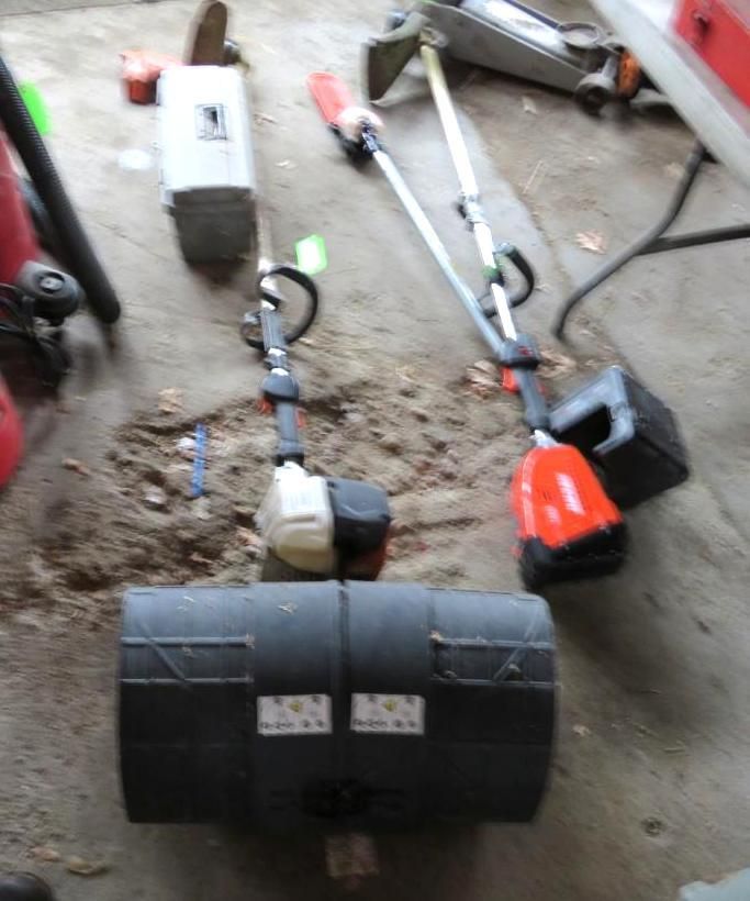 Two string trimmers and a lawn roller on a concrete surface.