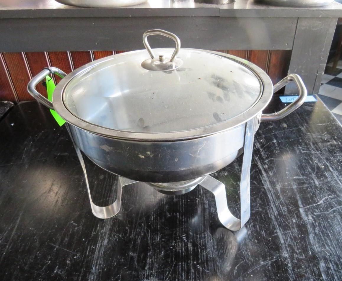 Stainless steel chafing dish with a glass lid on a dark tabletop.