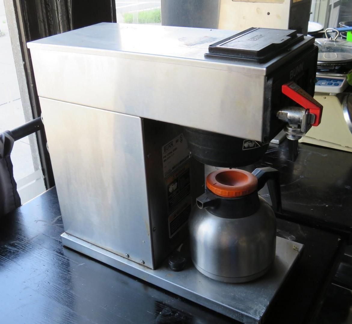 Stainless steel commercial coffee maker with a carafe on a black surface.