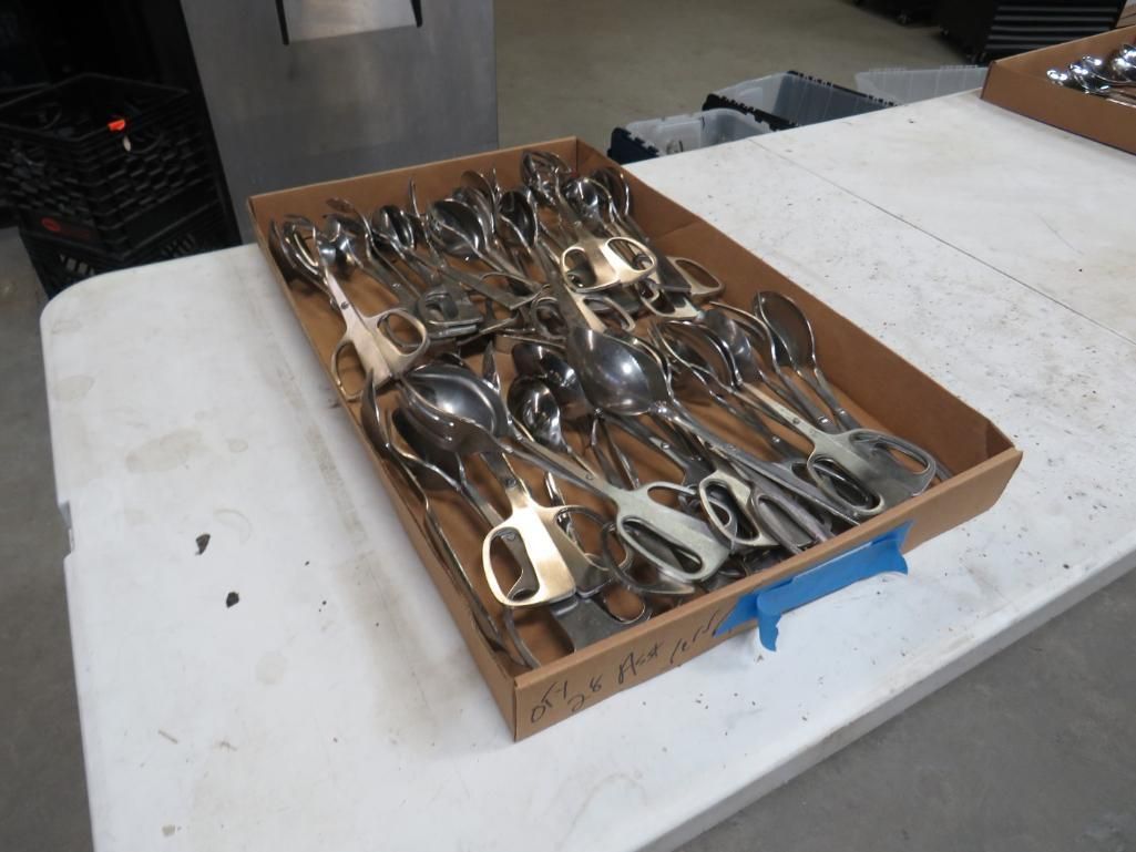 A cardboard box filled with silver serving spoons and tongs on a white table.