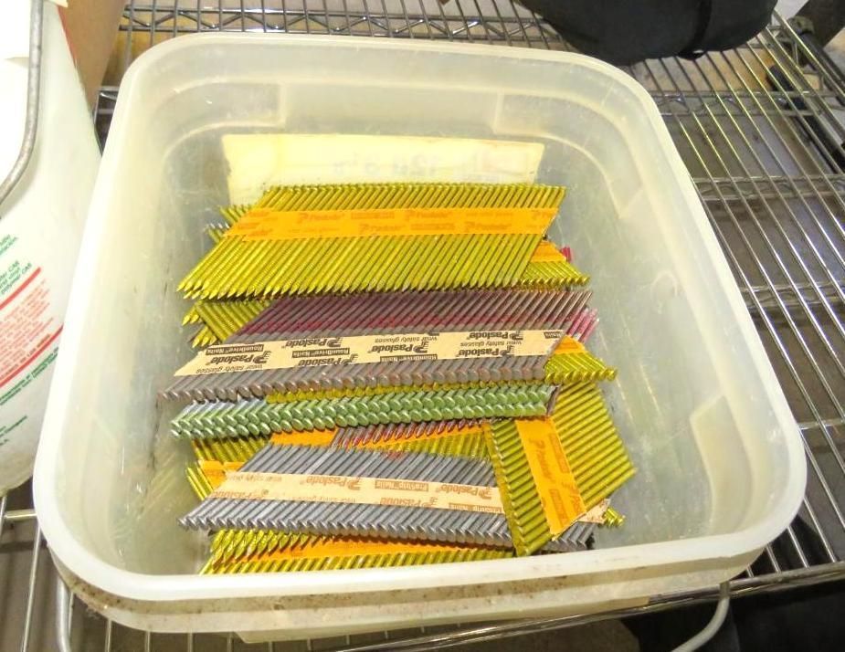 Nail gun cartridges in a clear plastic bin on a shelf. Cartridges are various colors: yellow, brown, and purple.