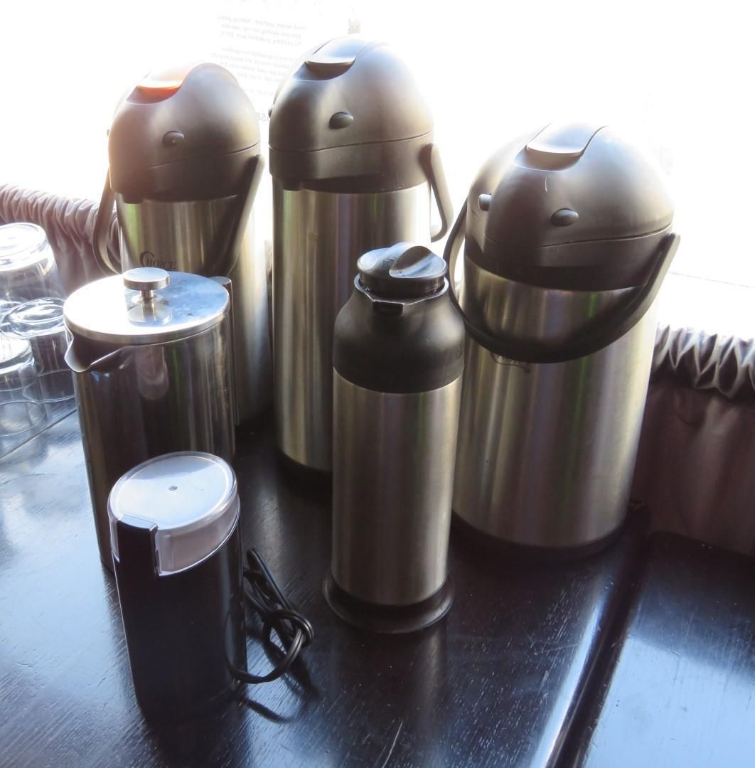 Silver and black insulated beverage containers on a dark surface, with a small coffee grinder in the foreground.
