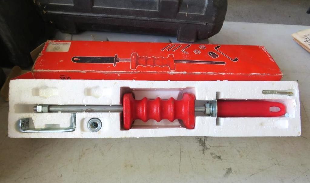 A red slide hammer tool kit in its red box, on a table.