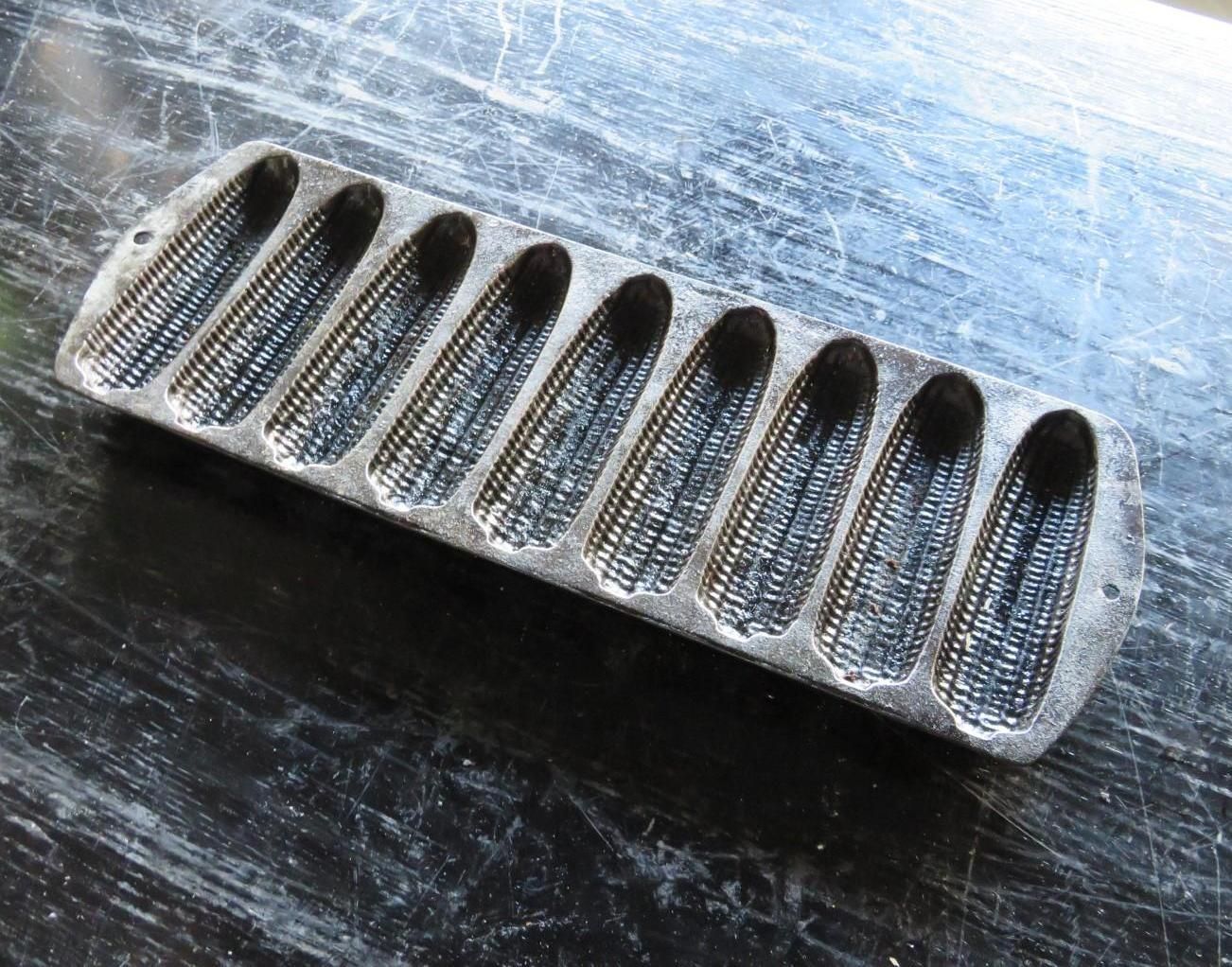 Cast iron cornbread pan with corn cob shaped molds on a dark, reflective surface.