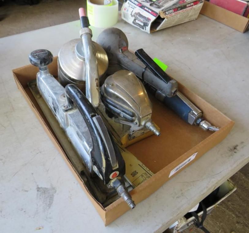 Tools in a cardboard box on a table, including sanders, grinders, and air tools.