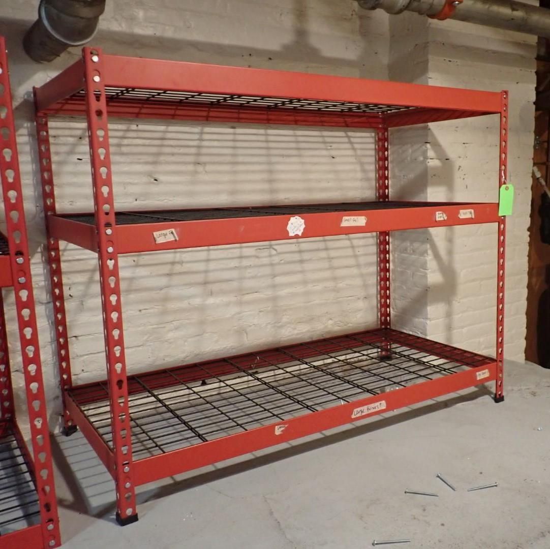 Red metal storage shelving in a basement. Three shelves, two solid and one wire mesh.