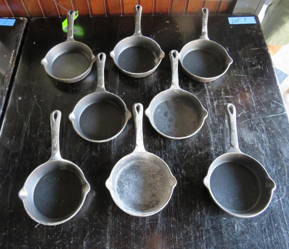 Eight small, dark cast iron skillets on a dark surface, arranged in two rows.