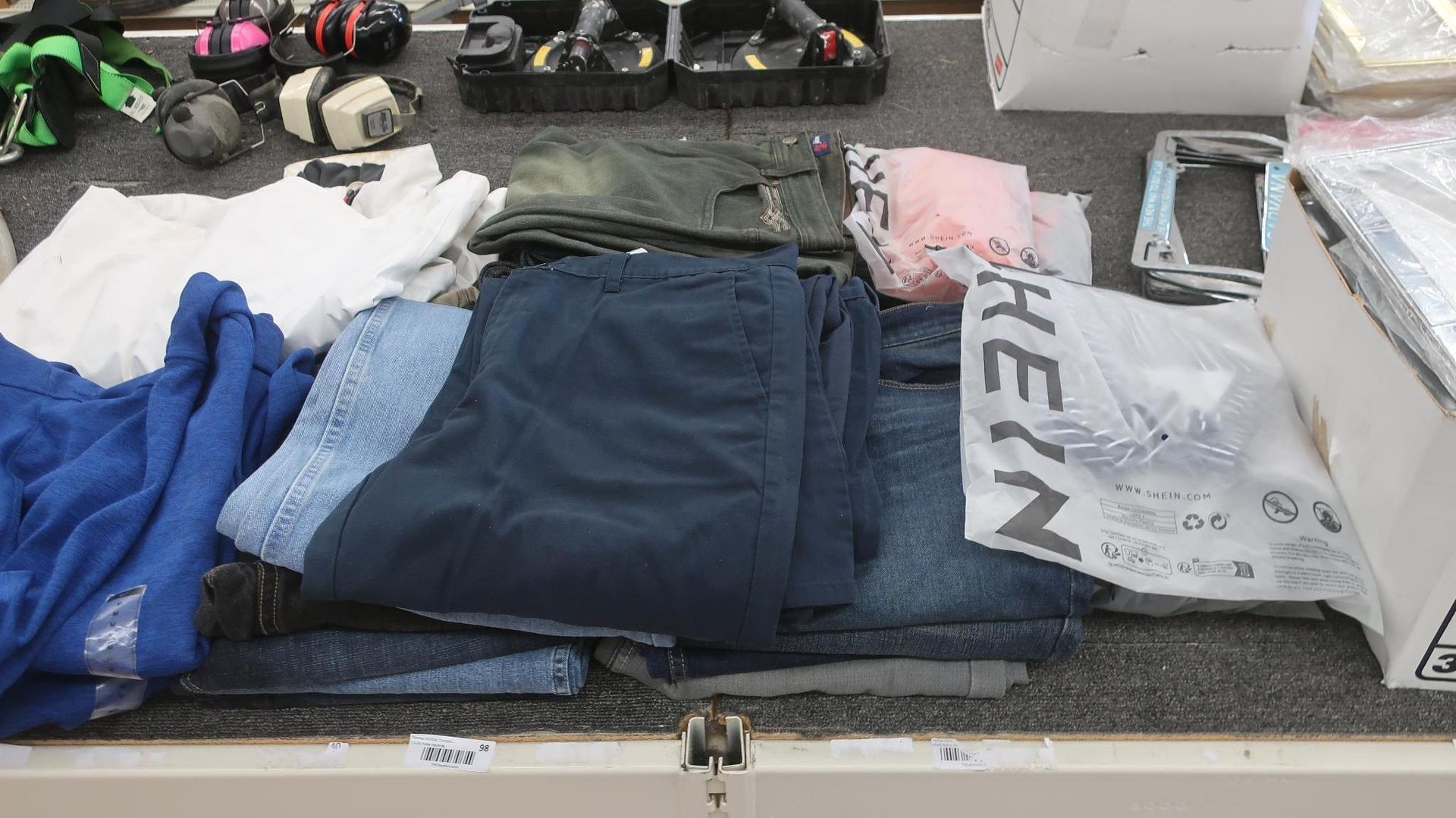Clothes and miscellaneous items laid out on a table, including folded pants, shirts, and a Shein bag.