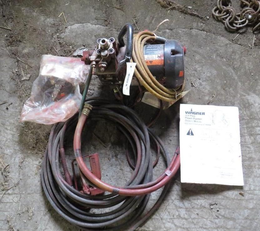 A WAGNER paint sprayer with hose, manual, and accessories, sitting on a concrete surface.