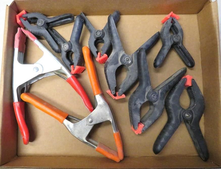 Box of assorted black and orange spring clamps with red tips.