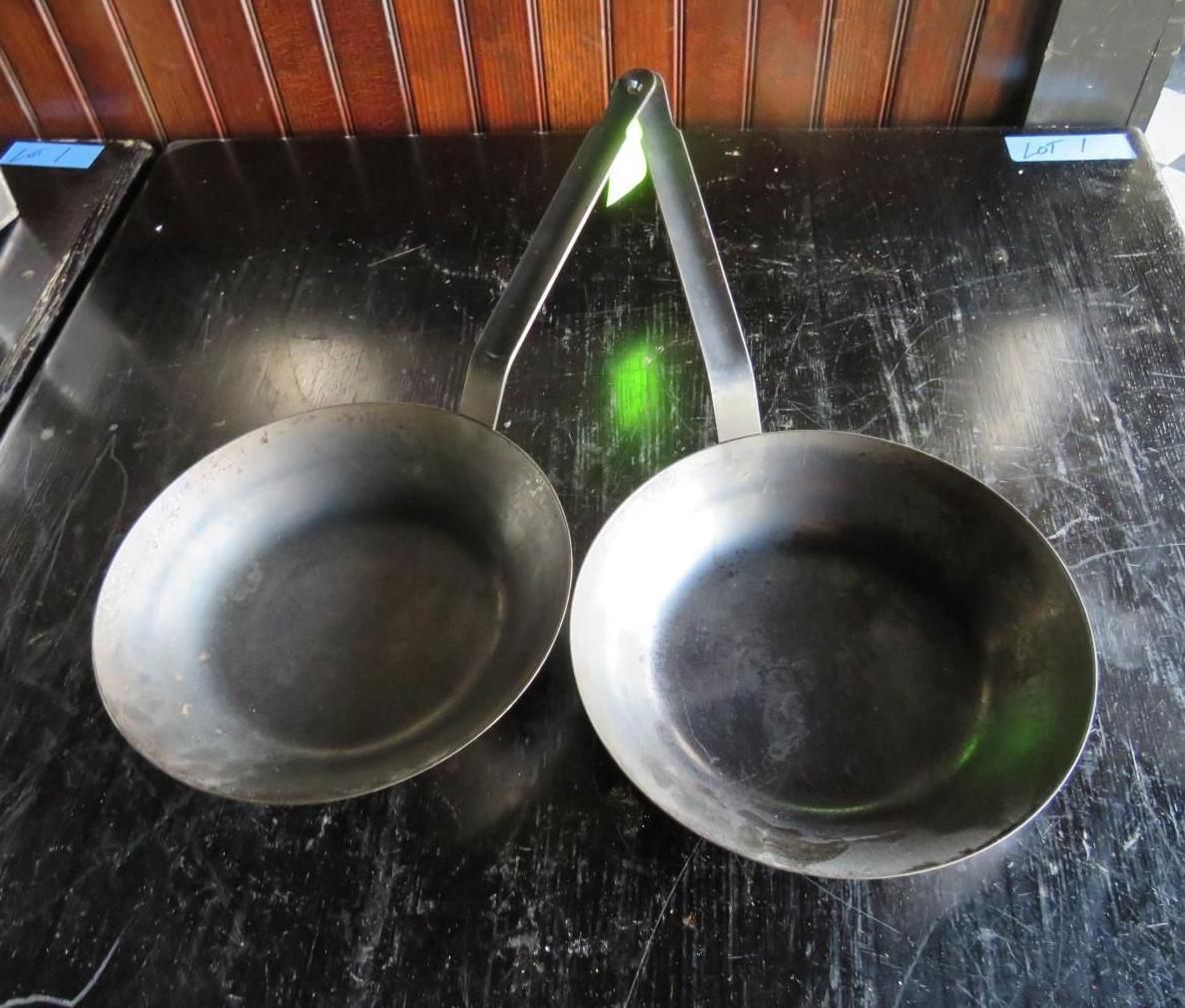 Two metal pans with long handles on a dark surface.