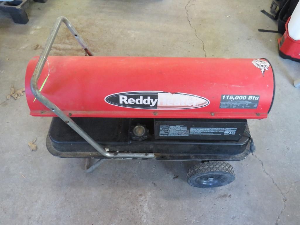 Red Reddy kerosene space heater, red cylinder, black base, handle, wheels on concrete.