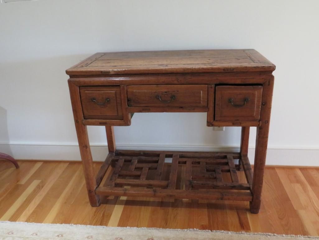 Wooden desk with drawers, ornate base shelf, set on a hardwood floor.
