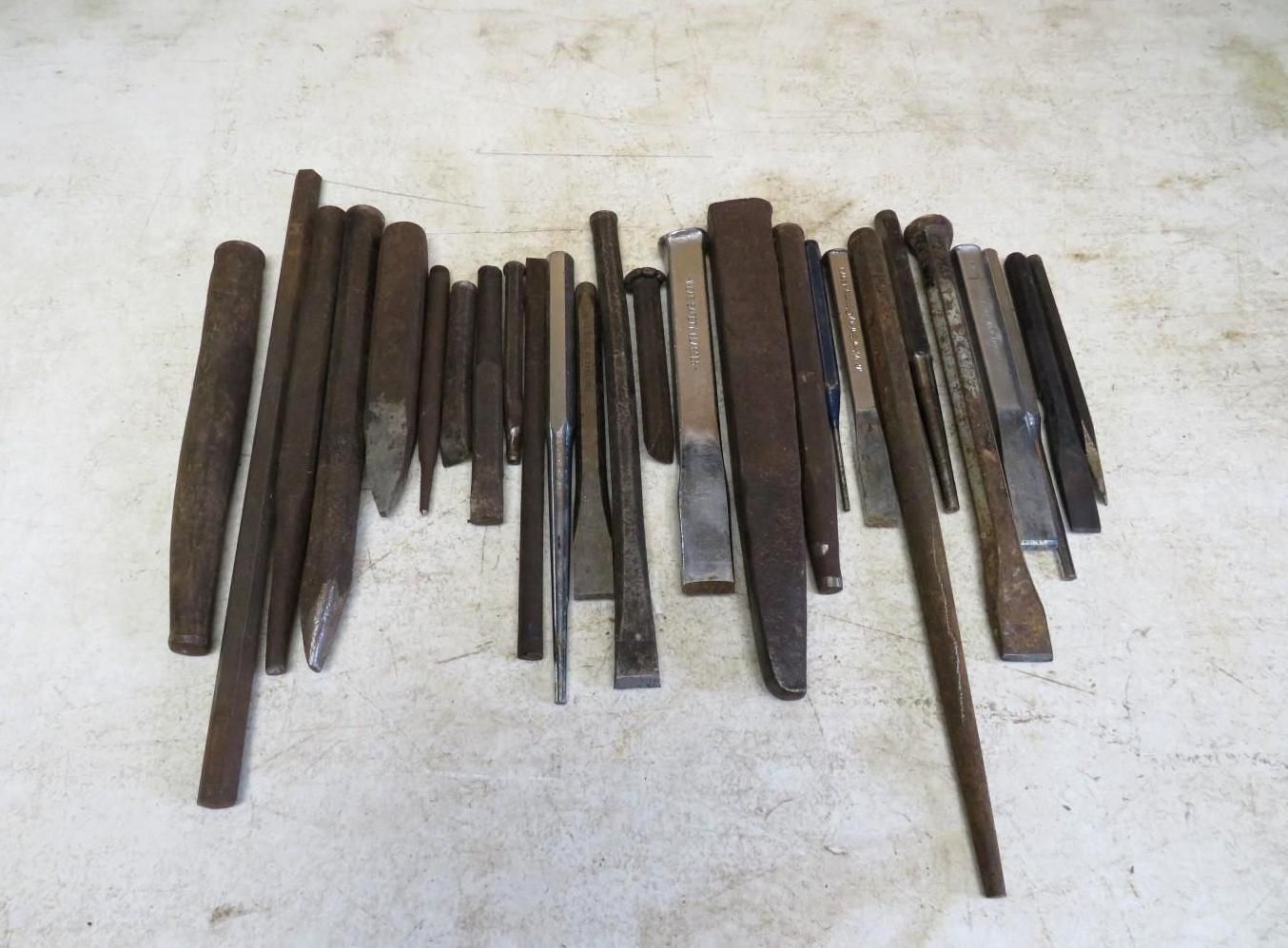 Collection of metal chisels and punches, various sizes, lying on a surface.