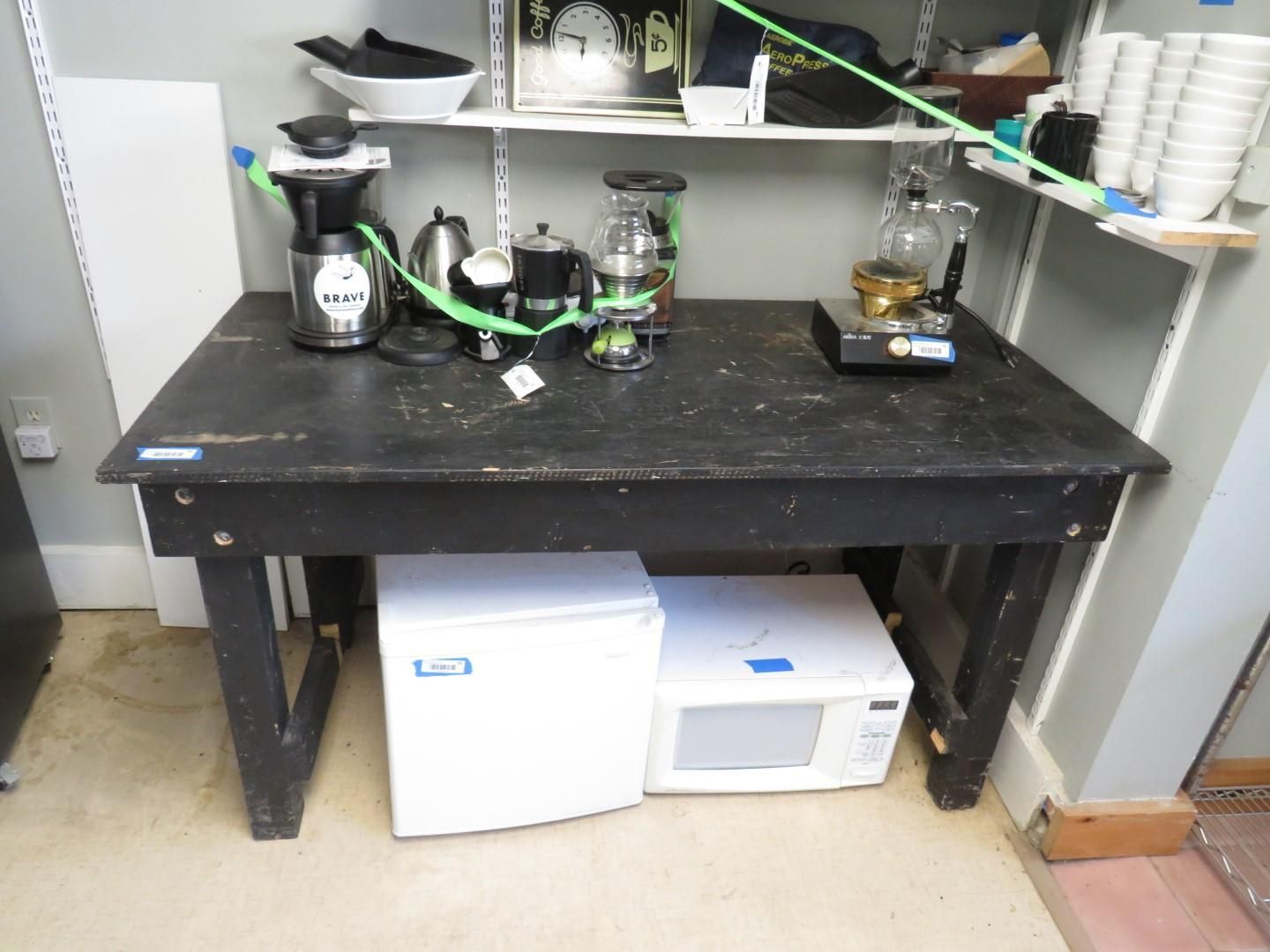 Black table with coffee makers, kettle, fridge, and microwave underneath. Shelves above.