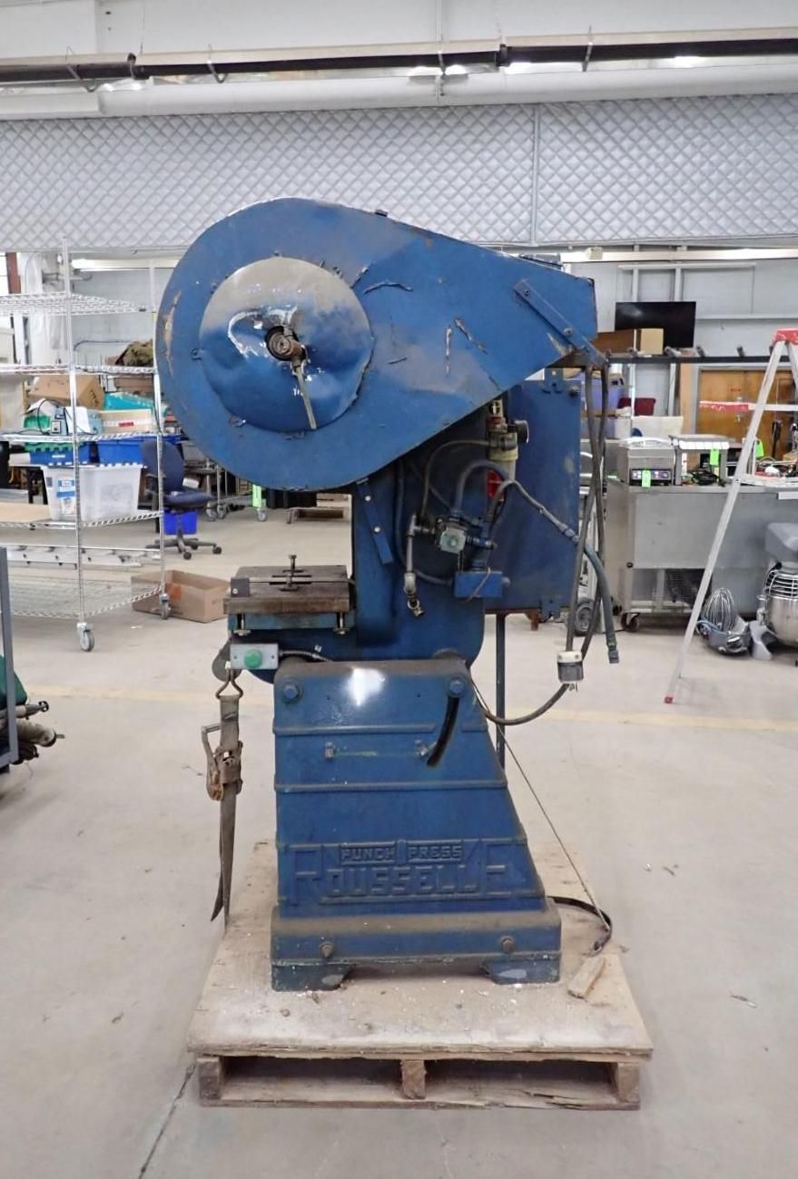 Blue industrial press machine on a wooden pallet in a workshop.