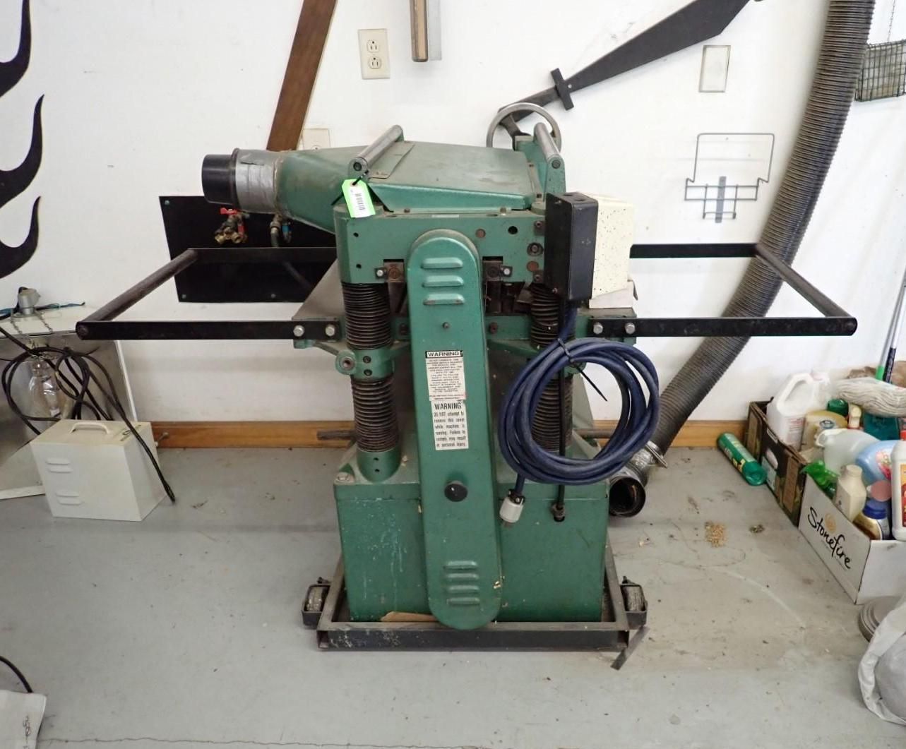 Green industrial woodworking planer on a gray concrete floor.