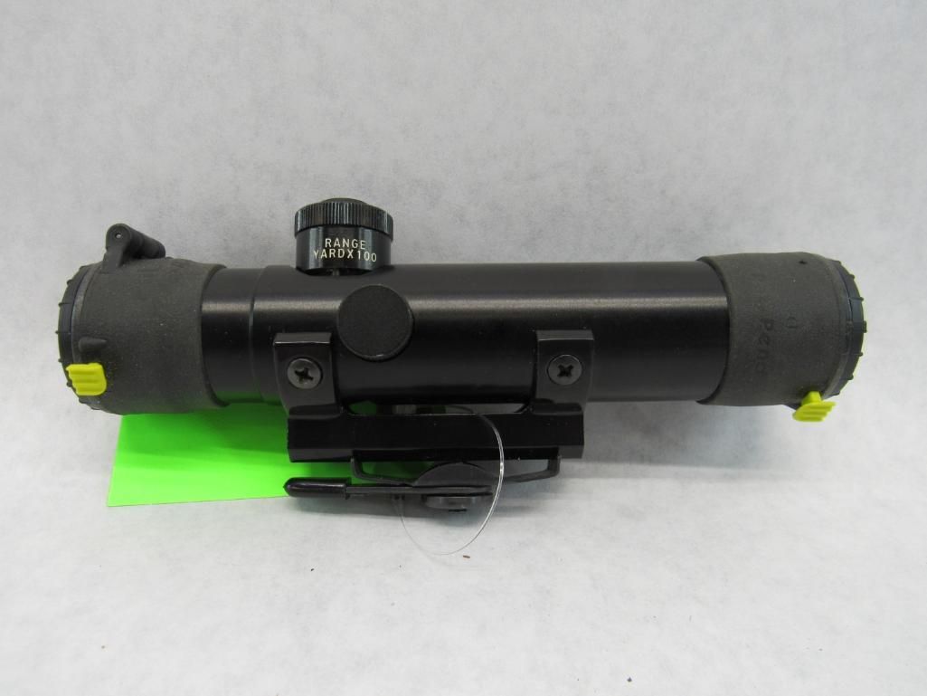 Black rifle scope with a built-in mount; yellow end caps and green sticker visible.