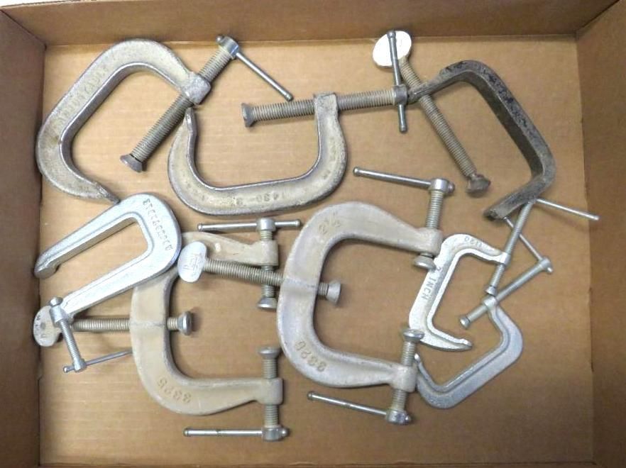 Assortment of C-clamps in a cardboard box, varying sizes, silver metal, with screw handles.