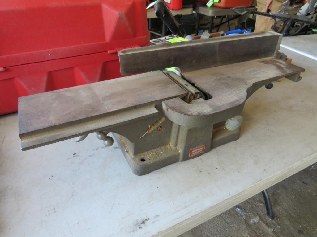 A Delta jointer sits on a table. It is gray, with wood surfaces and a red label.