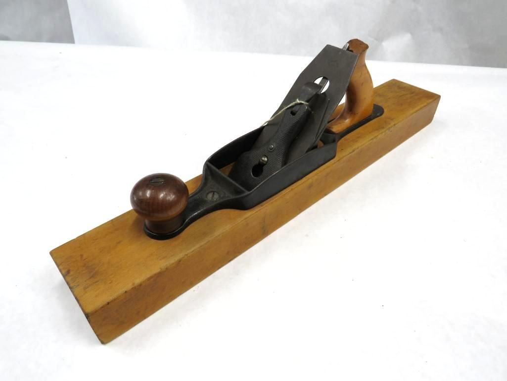 Wooden smoothing plane with black metal components, brown handles, on a white surface.