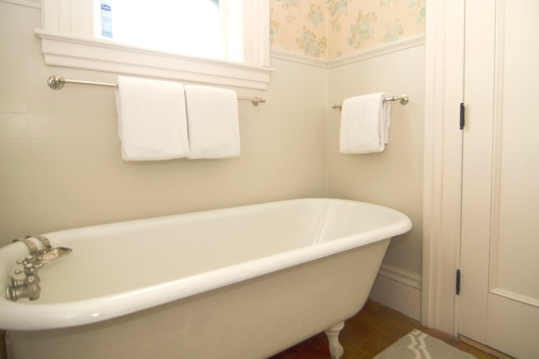 Clawfoot bathtub with two white towels hanging nearby in a cream-colored bathroom.