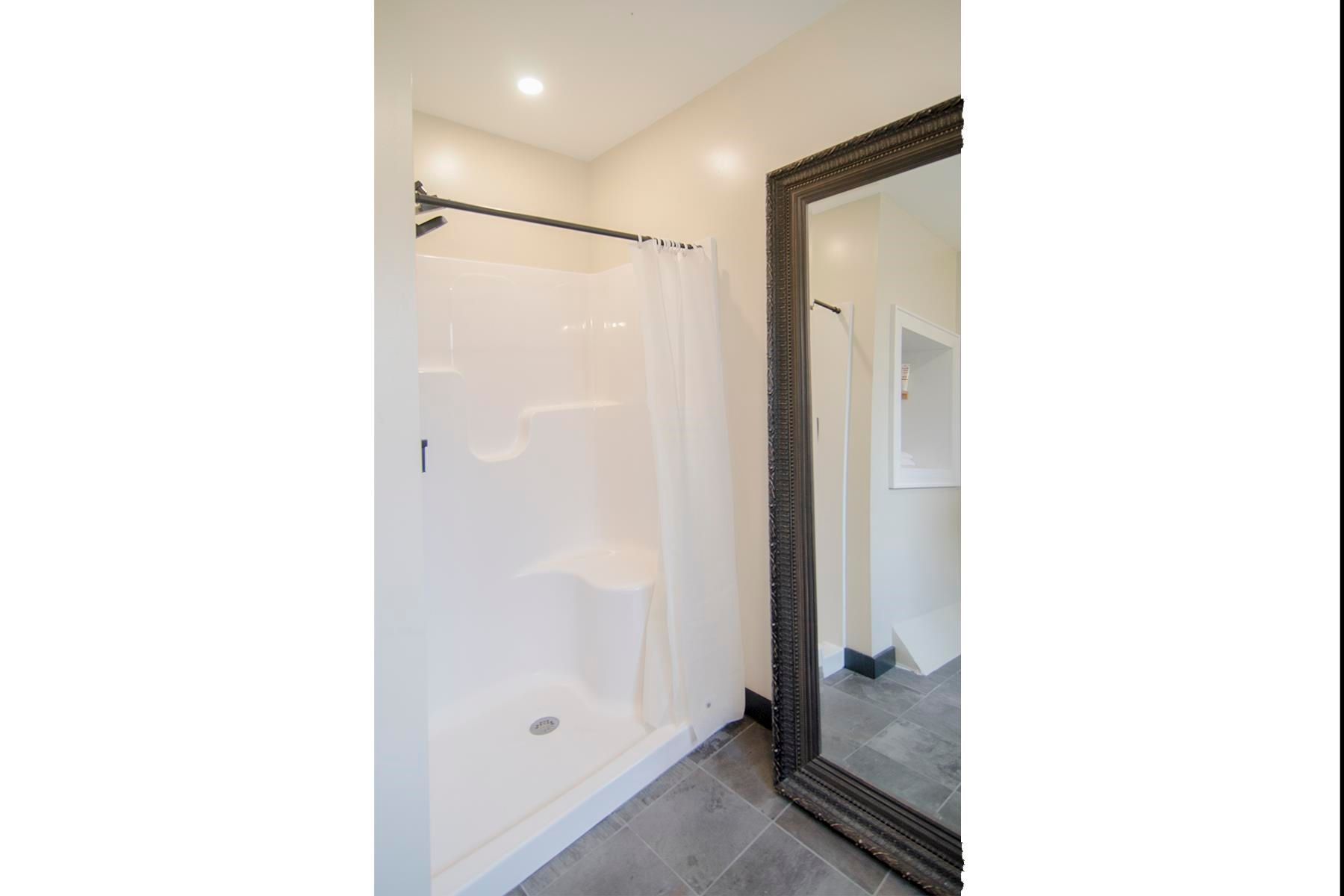 White shower stall with a curtain and a large mirror with a dark frame in a bathroom.