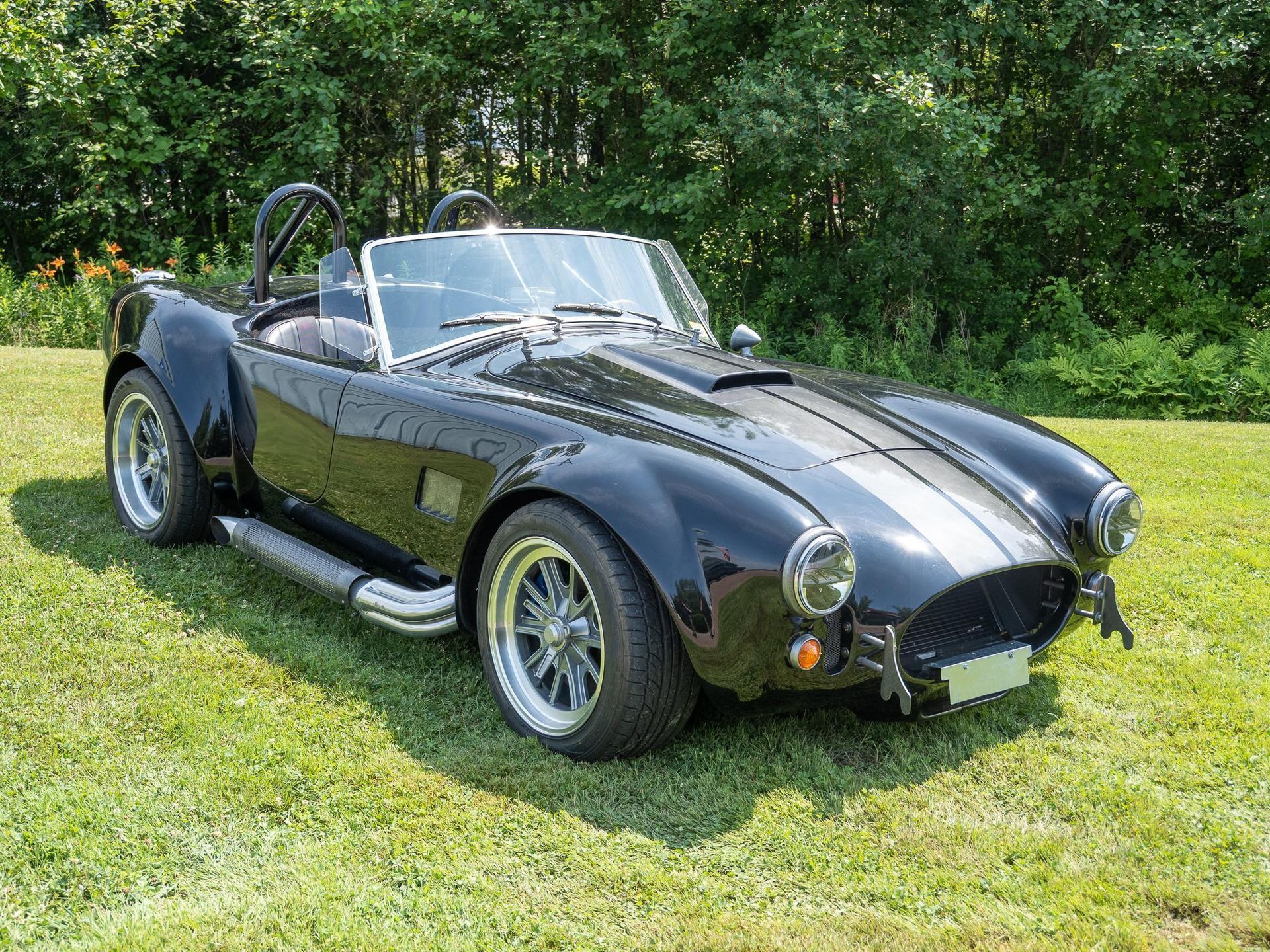 Black and silver sports car, a Shelby Cobra replica, parked on a grassy lawn.