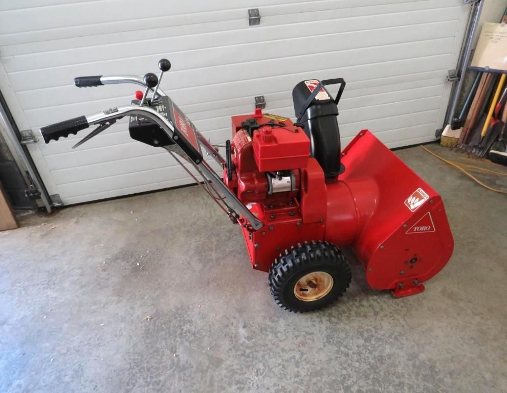 Red snowblower on a concrete floor in front of a white garage door.