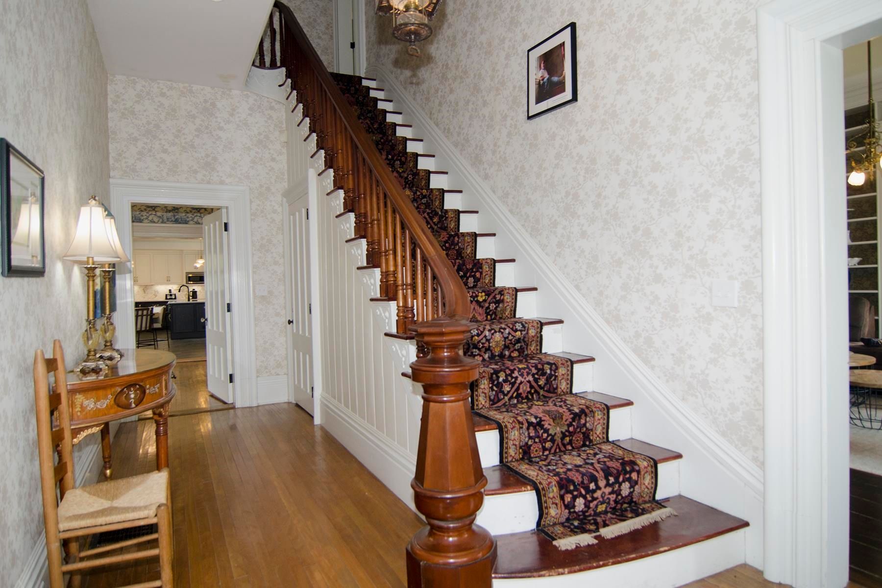 Wooden staircase in a home entryway with wallpaper and patterned runner.