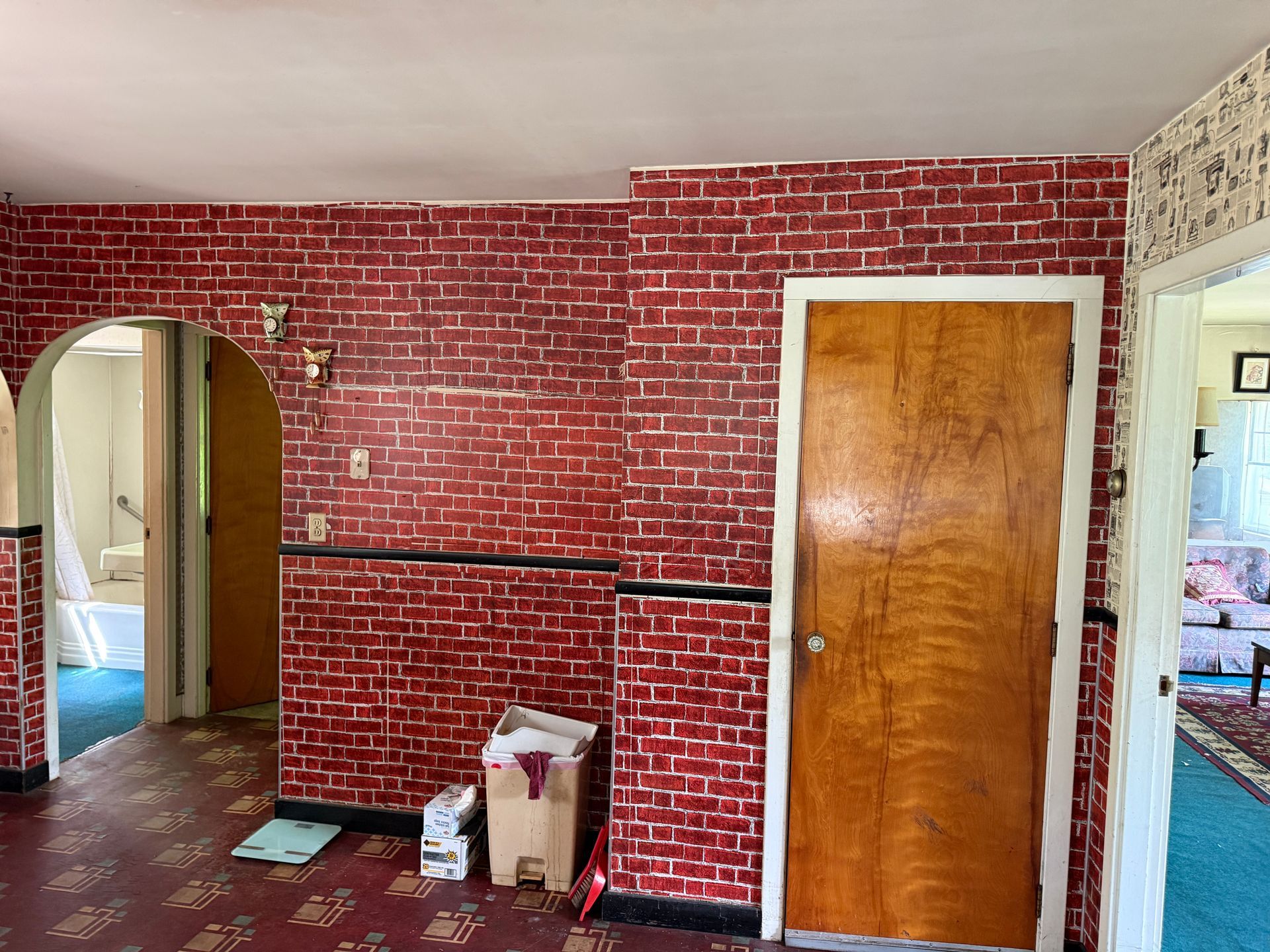 Red brick-pattern wall with a wooden door, white ceiling, and an open doorway into another room.