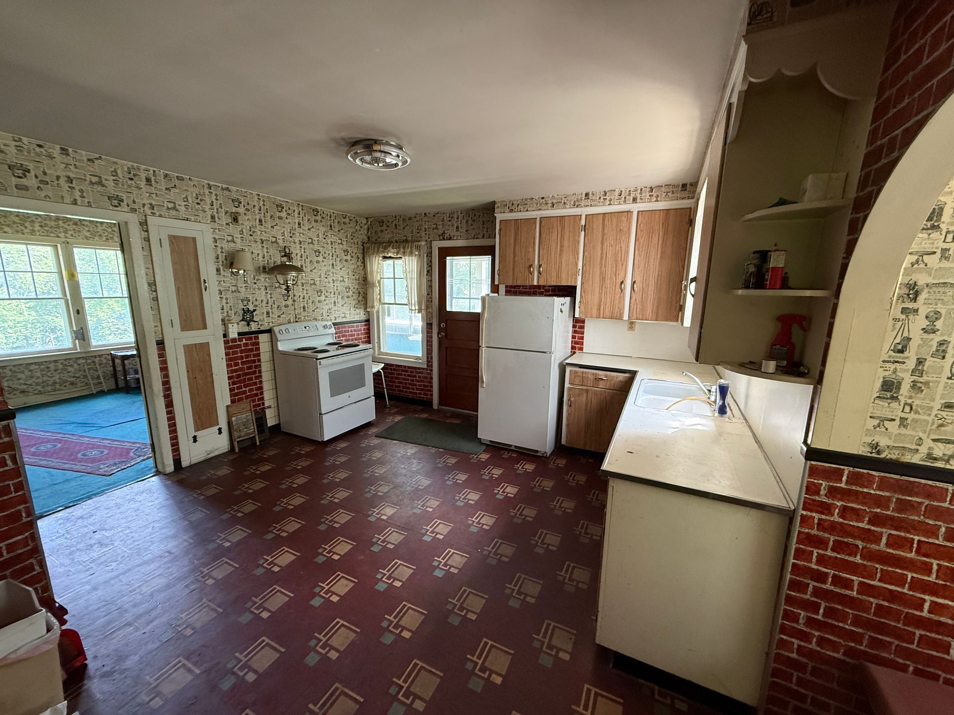 Empty kitchen with red patterned floor, white appliances, and wood cabinets, viewed from the dining area
