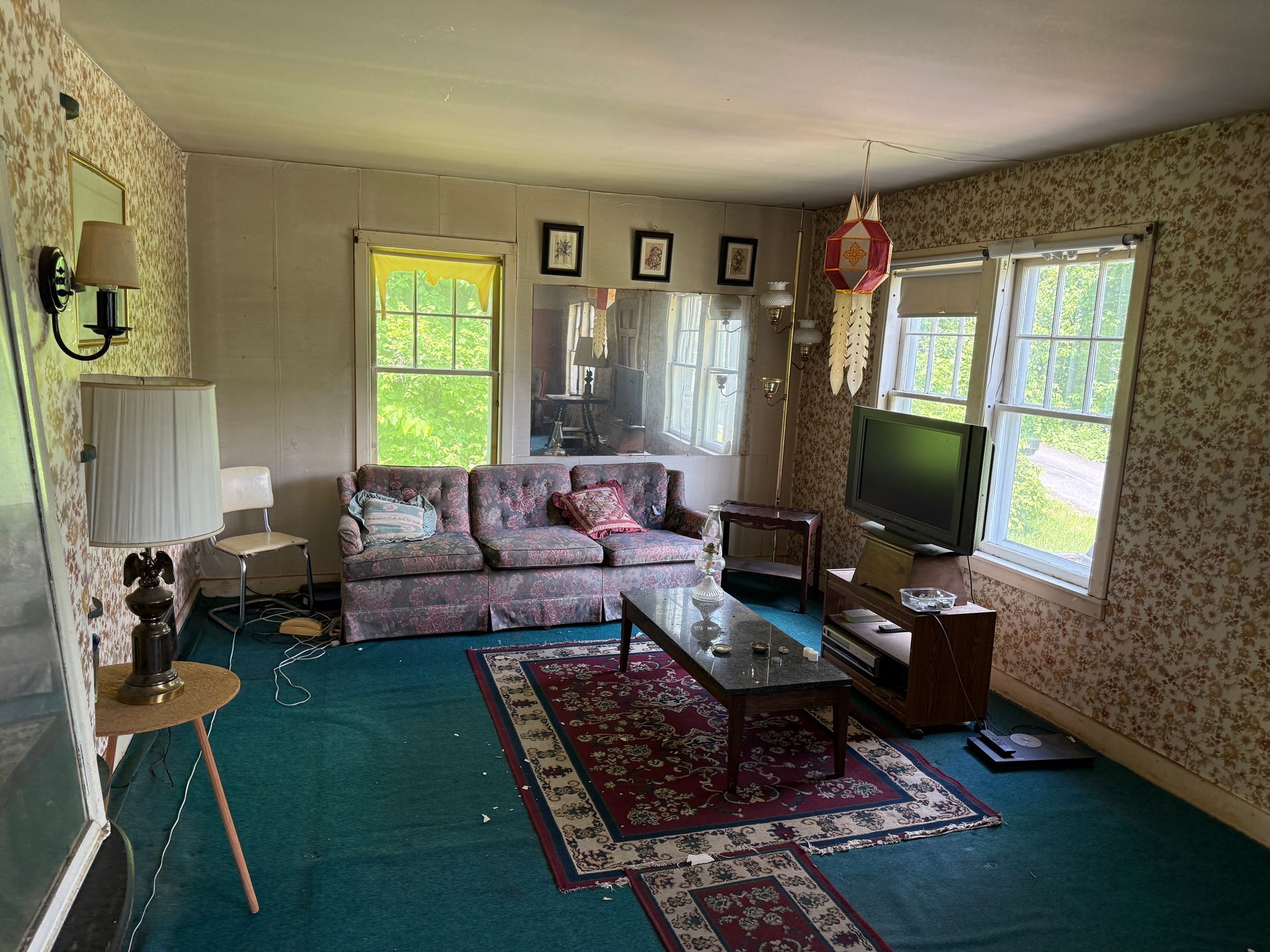 Living room with teal carpet, floral sofa, coffee table, TV, and bright windows