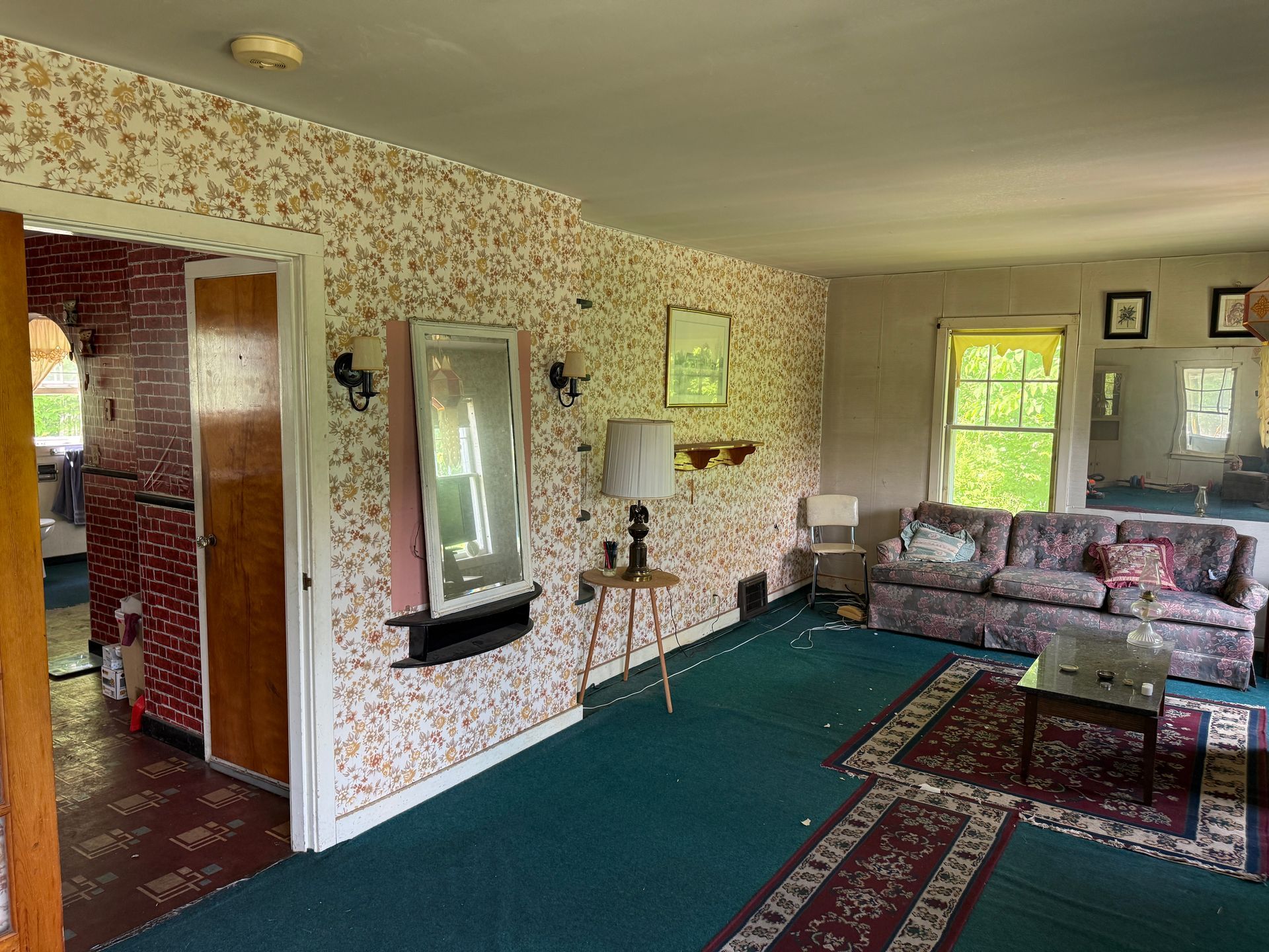 Living room with patterned wallpaper, green carpet, sofa, mirror, and front door view