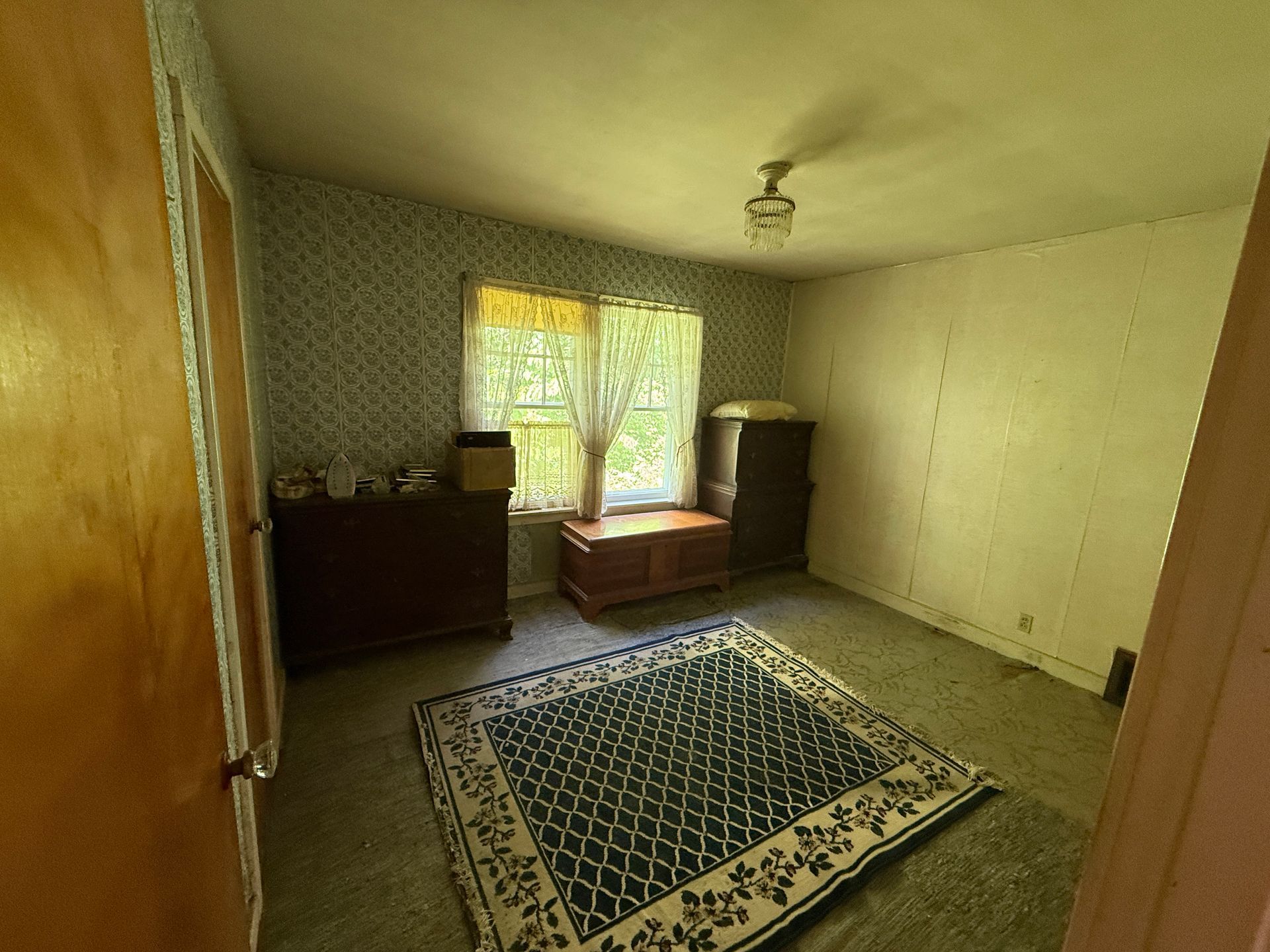 Empty bedroom with patterned rug, dresser, window light, and plain cream walls