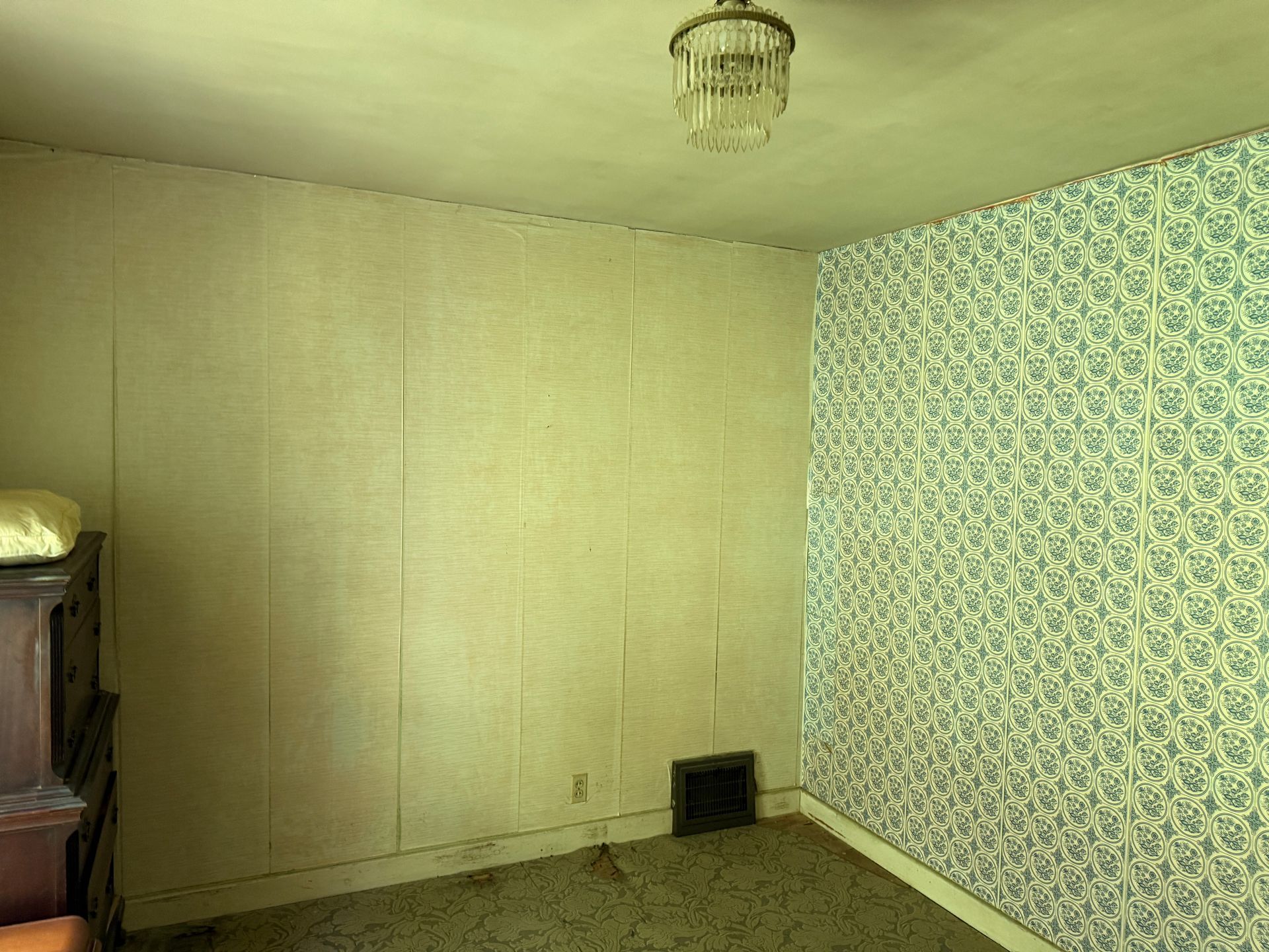 Empty room with beige walls, patterned wallpaper, carpet, and a small chandelier ceiling light.