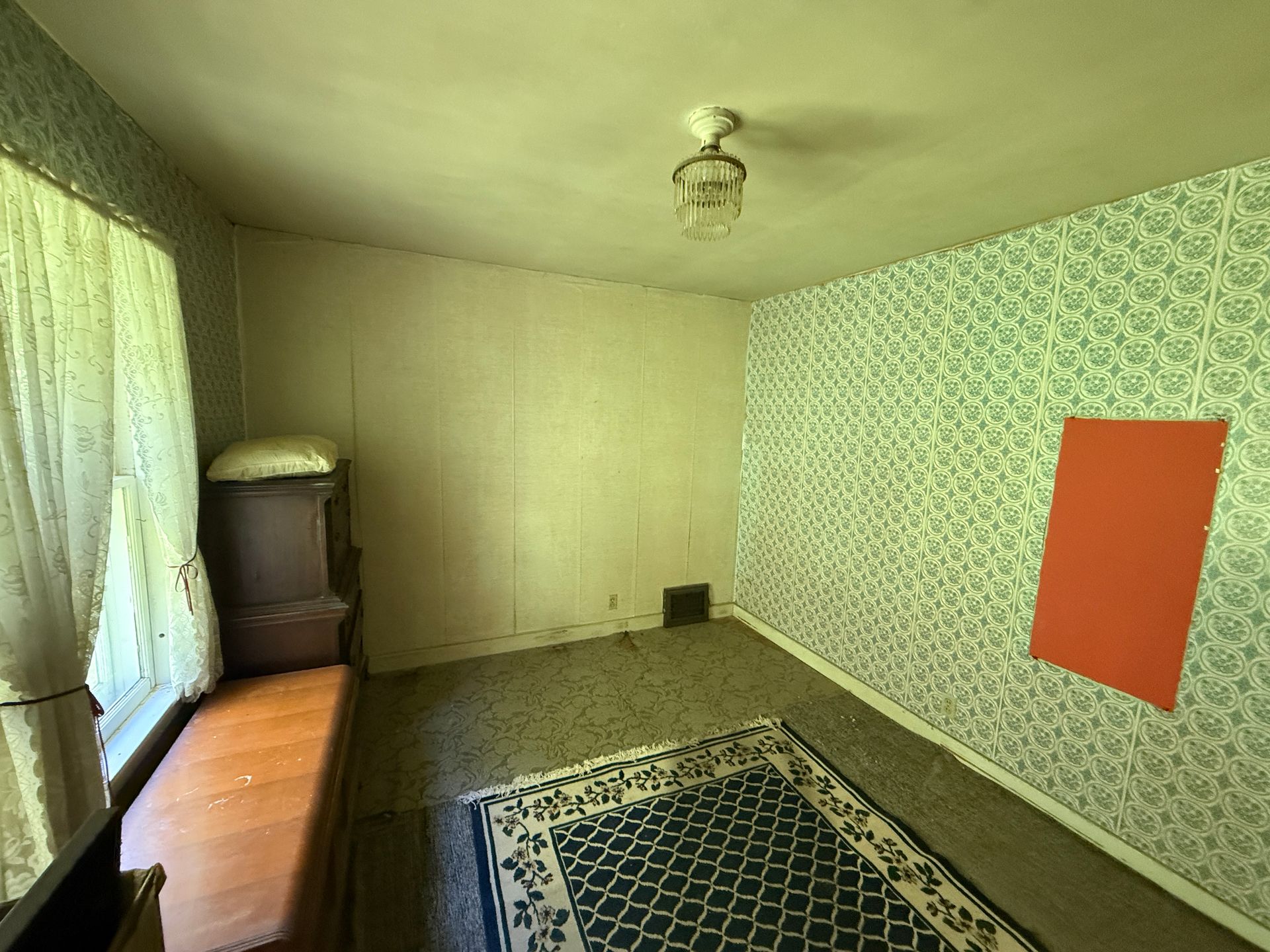 Empty living room with patterned rug, patterned wallpaper, window with curtains, and orange wall panel.