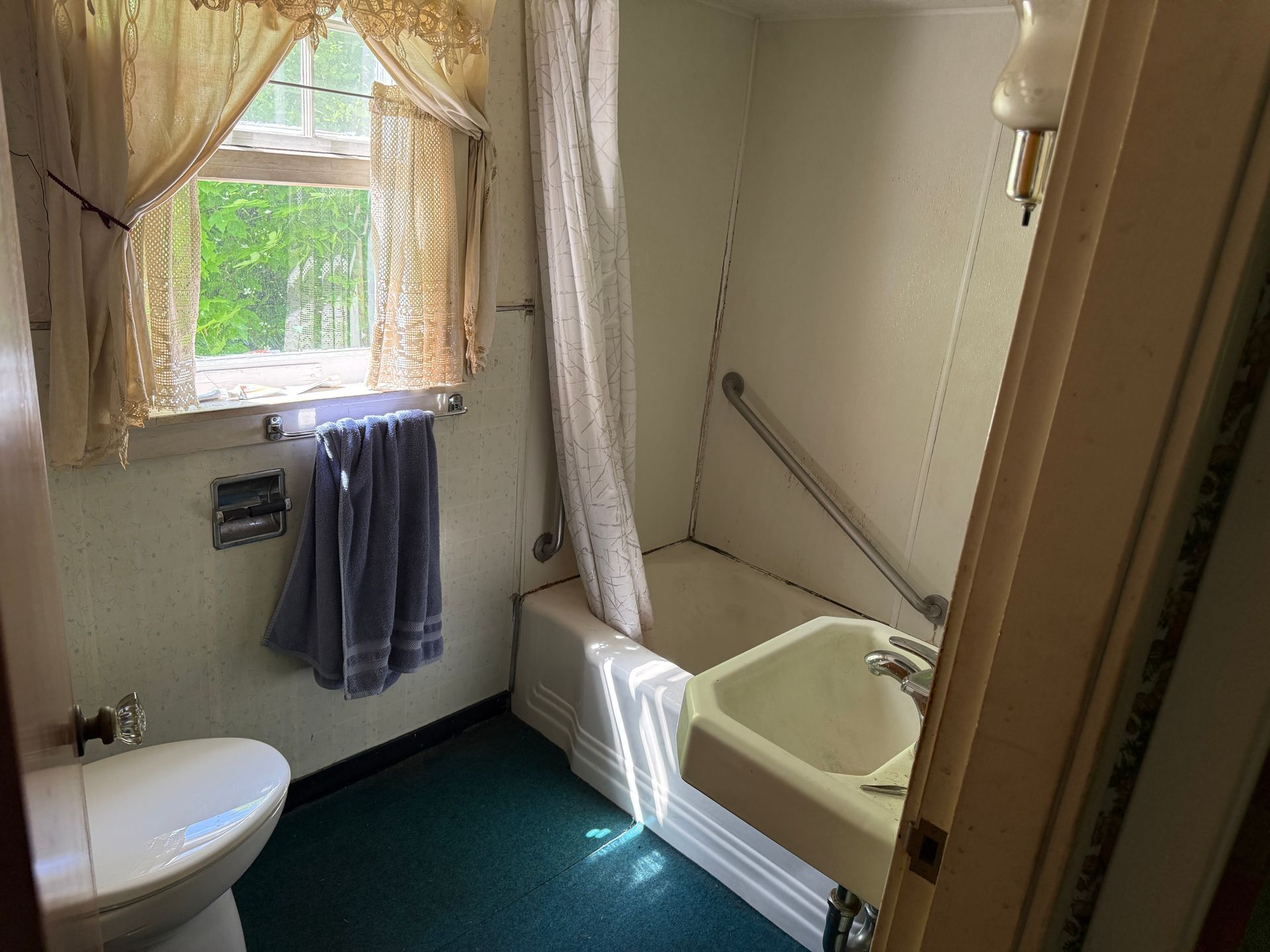 Small bathroom with a window, toilet, tub, towel rack, and green floor.