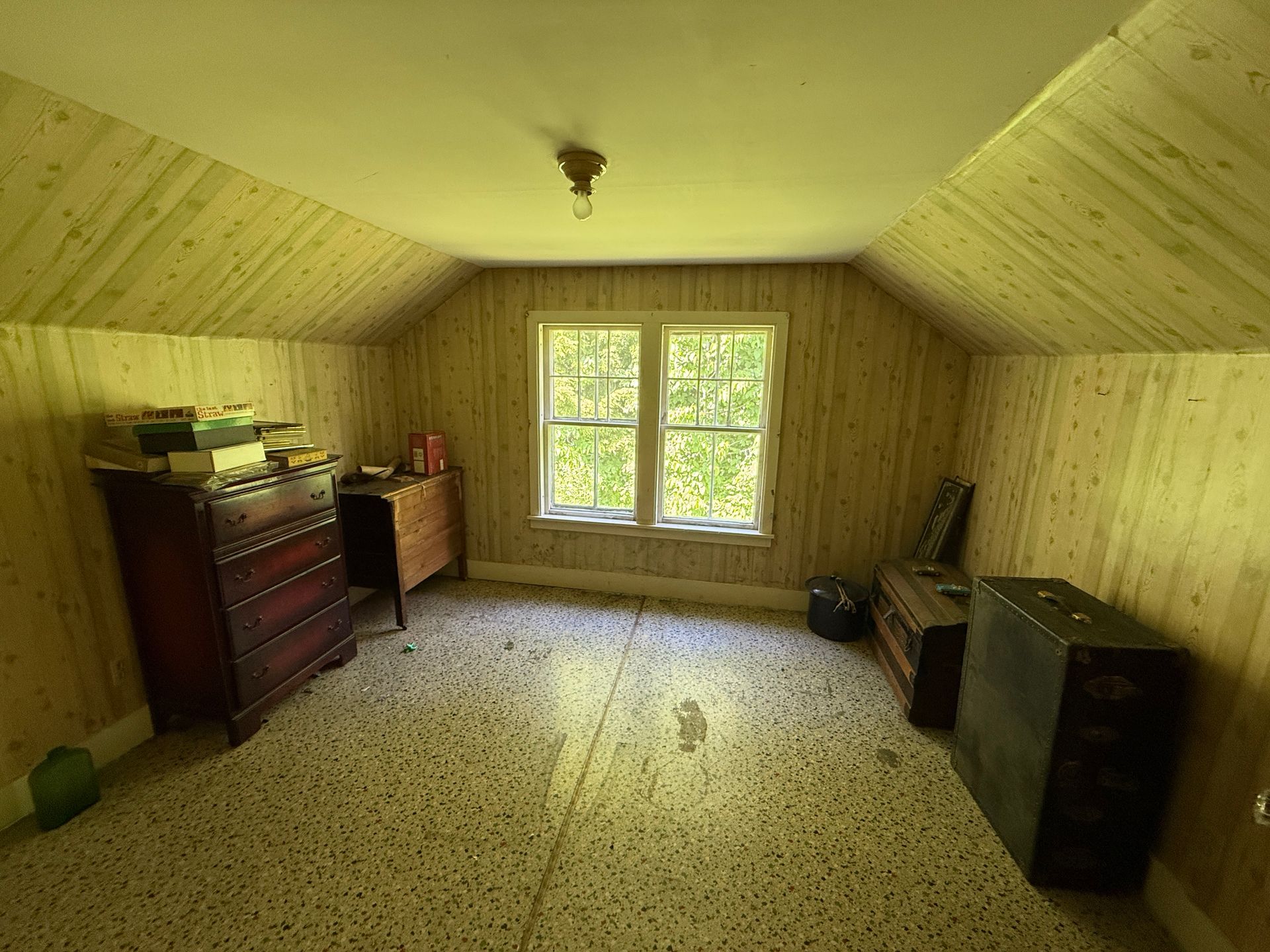 Small empty attic room with wood-paneled walls, a window