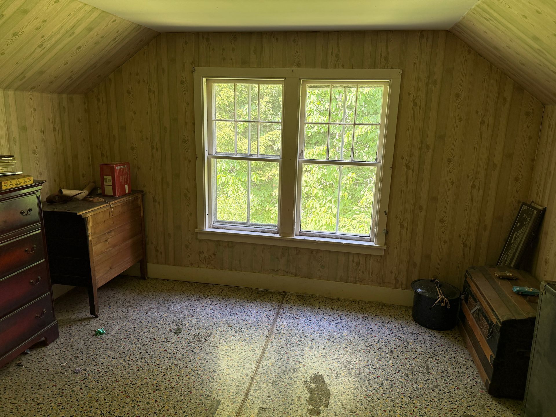 Small wood-paneled attic room with a window, carpeted floor, dresser, and bench.