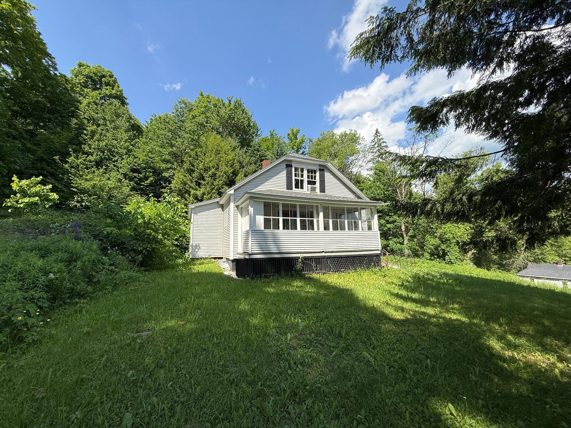 Small white cottage on a grassy hill surrounded by trees under a blue sky