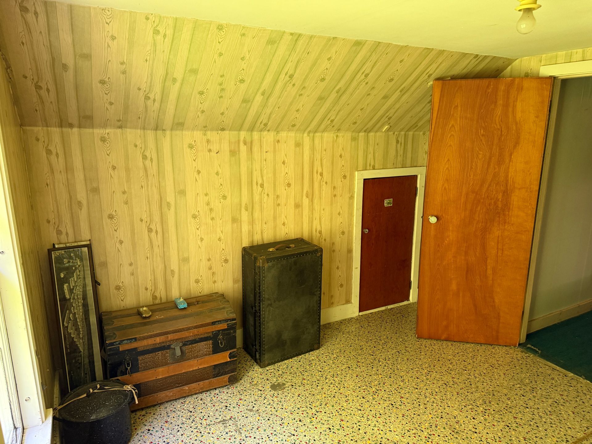 Empty room with patterned carpet, wood-paneled walls, dresser, cabinet, and a red door.