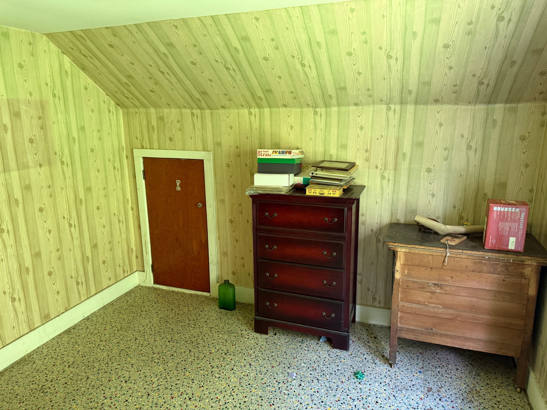Empty attic room with slanted green wallpaper, carpet, a wooden door