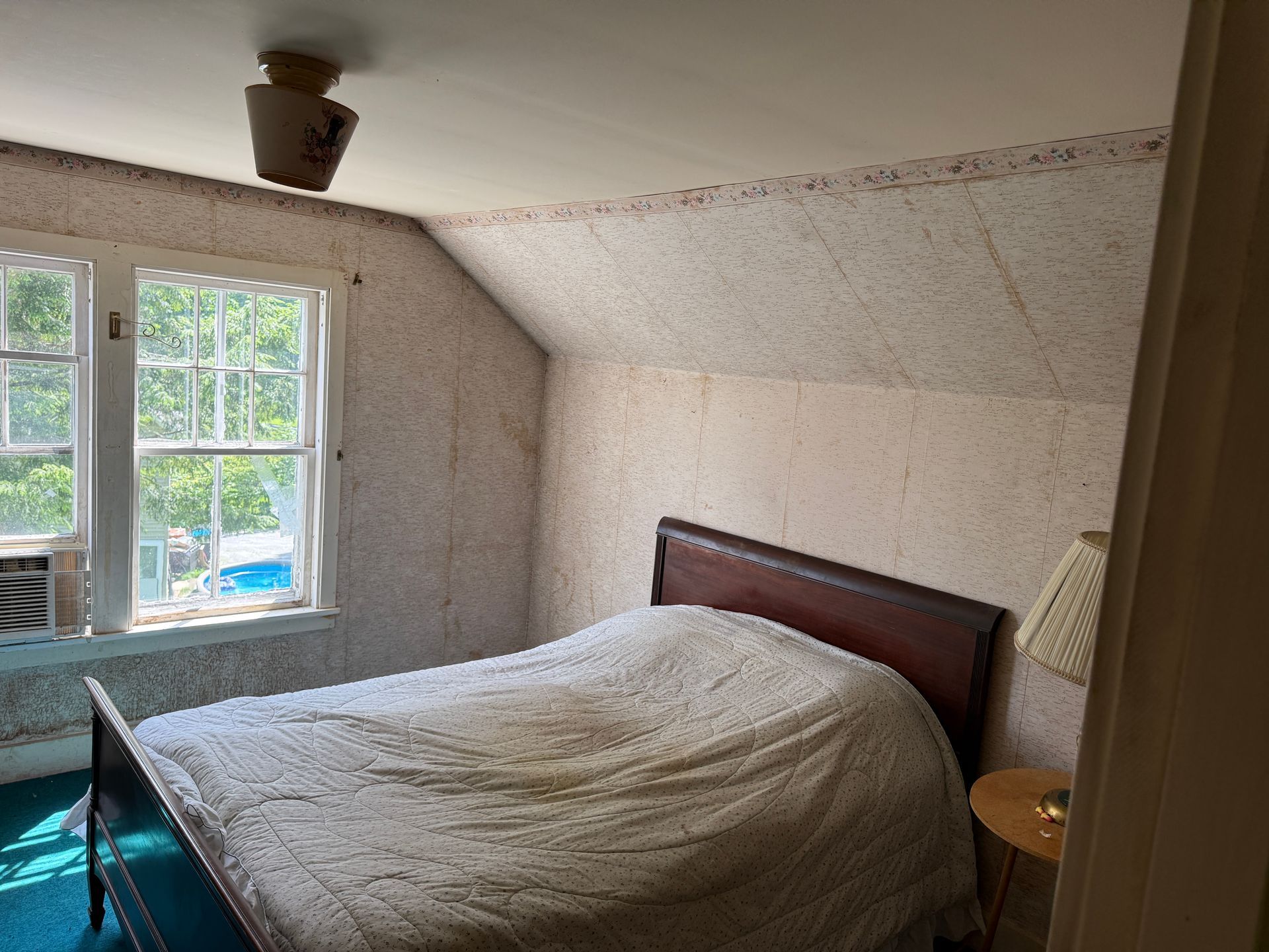 A small bedroom with a bed, window, lamp, and sloped ceiling.