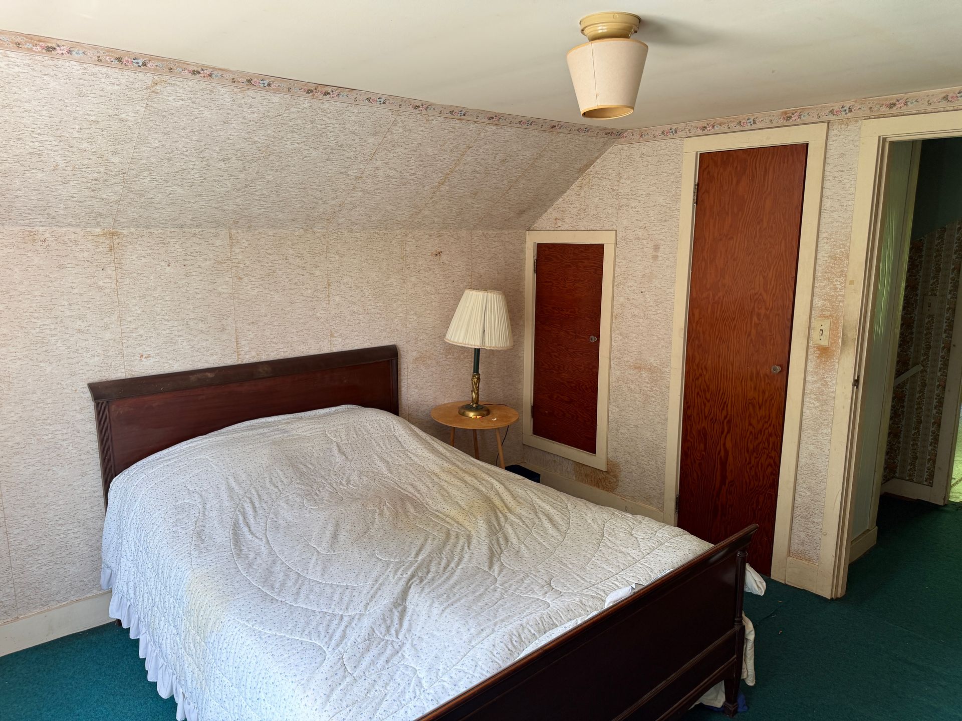 Small bedroom with a bed, nightstand lamp, and wood doors beside an open closet.