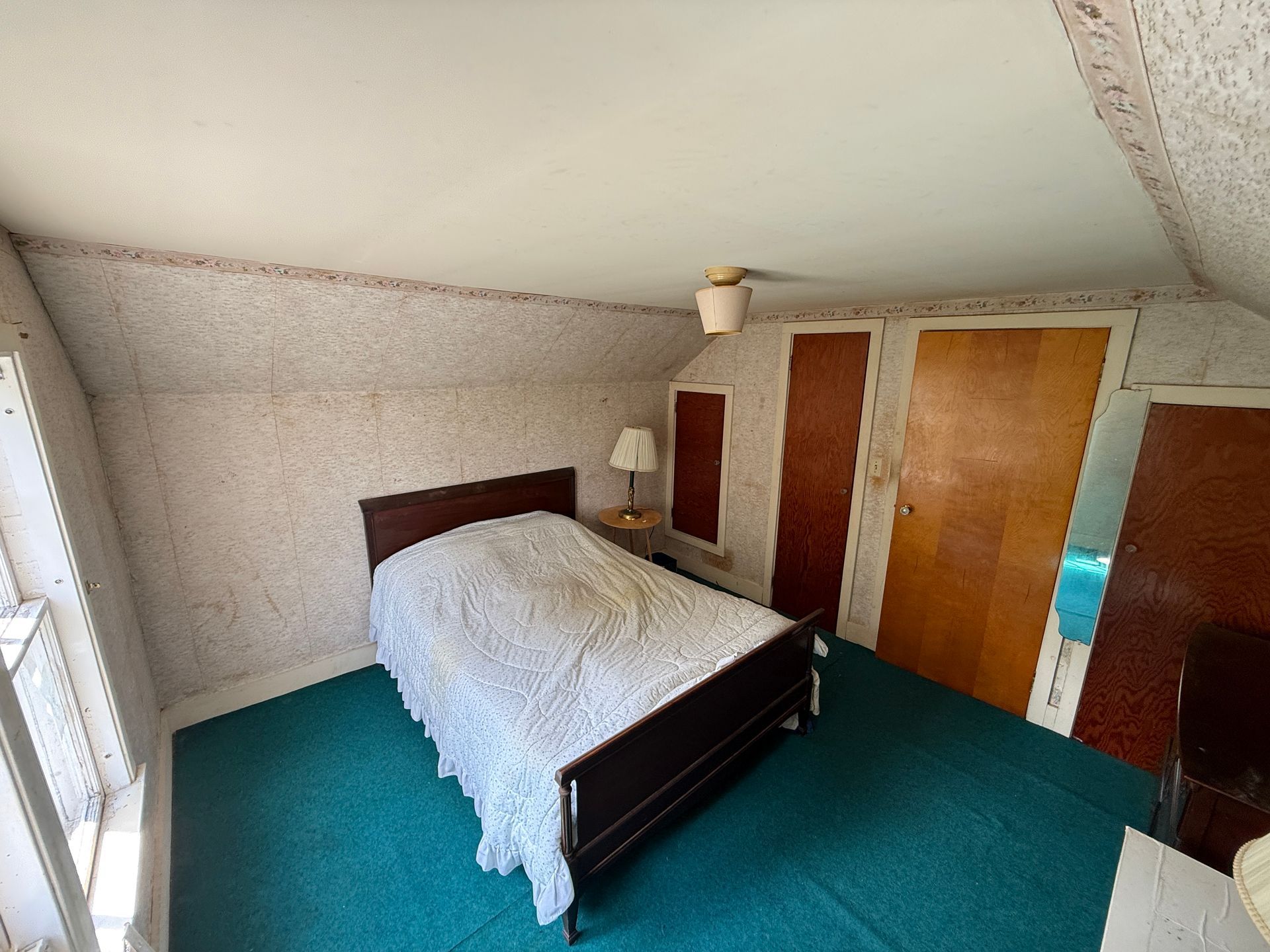 Small bedroom with a bed, white blanket, teal carpet, and closet doors
